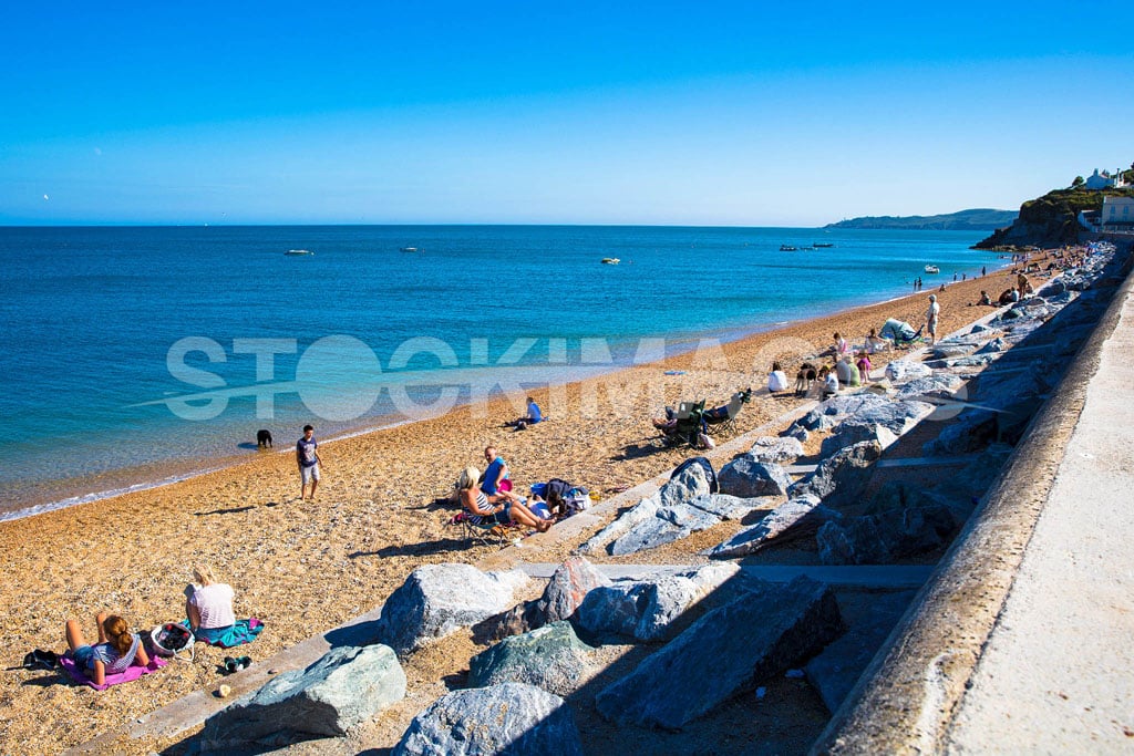 Vibrant image of visitors enjoy the sunshine at Torcross Beach in the Summer, with Start Point Lighthouse in the background.