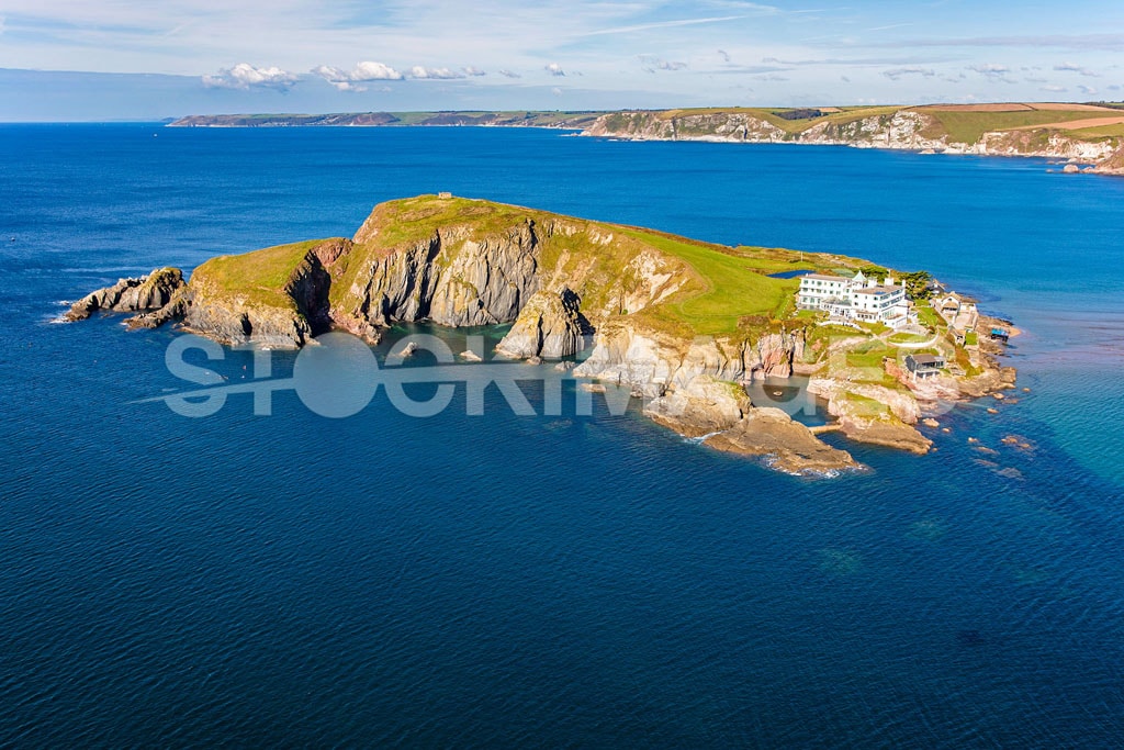 Aerial view of Burgh Island isolated in the surrounding high tide and vibrant blue sea, showing the front of the popular Burgh Island Hotel in the Summer.