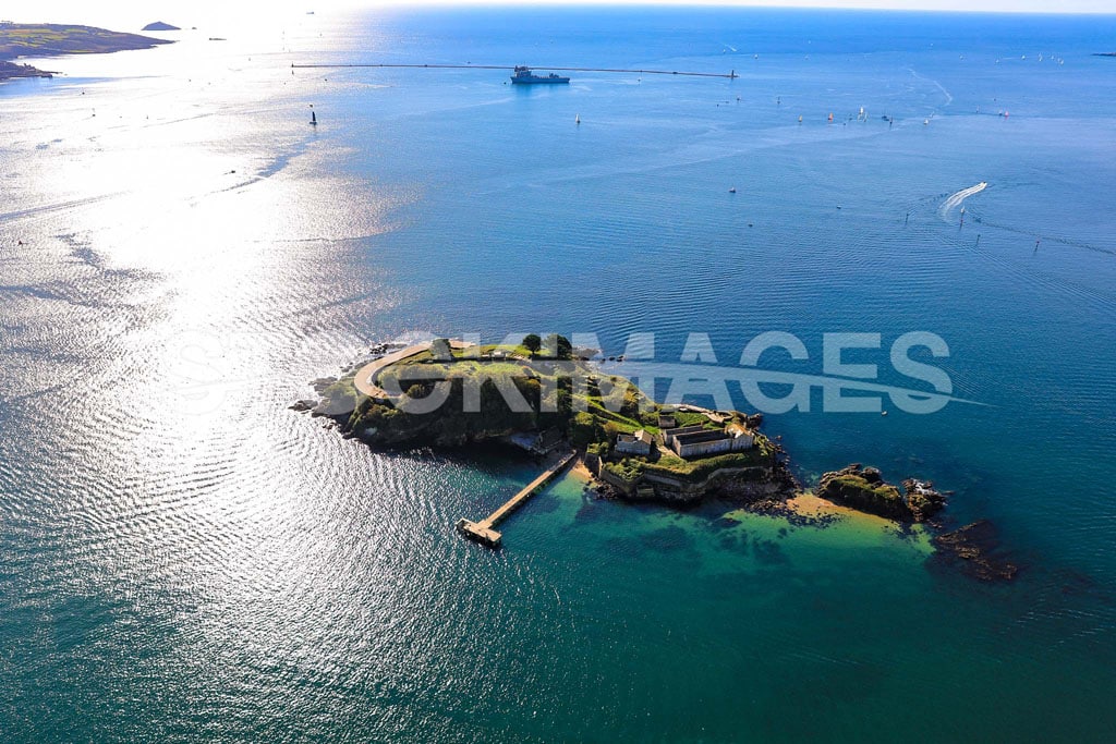 Aerial image of Drake's Island, Plymouth, with sun shimmering on the surrounding blue water and Plymouth Breakwater in the background.