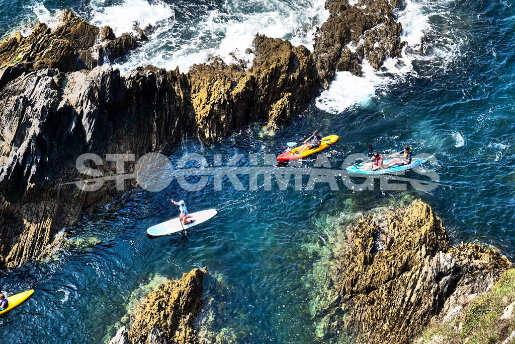 Visitors enjoying kayaking and paddleboarding around the rocks on the south side of Burgh Island Bigbury-on-Sea on the glistening, deep blue water.