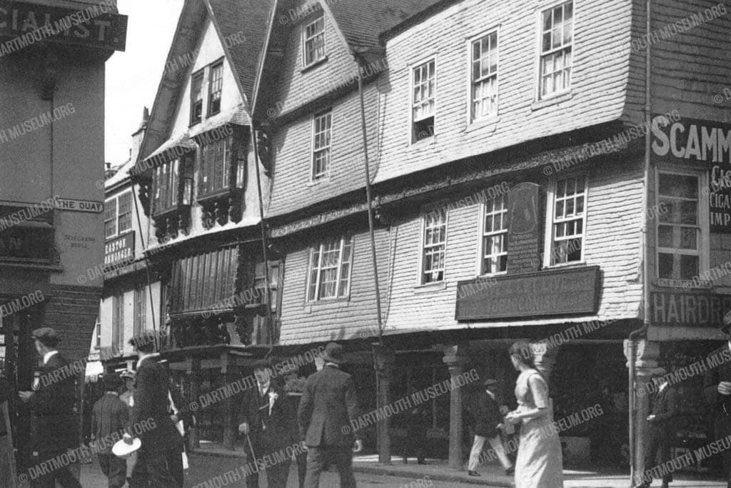 Historical photograph of a busy scene at Dartmouth's Butterwalk on the corner of the Quay between 1909 - 1914, showing the present Dartmouth Museum building.