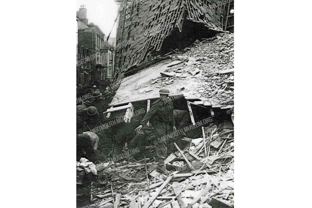Historical photograph of helmeted Army, Naval and Civillian personnel searching amoungst the ruins for survivors in Duke Street after the bombing in Dartmouth, February 1943.